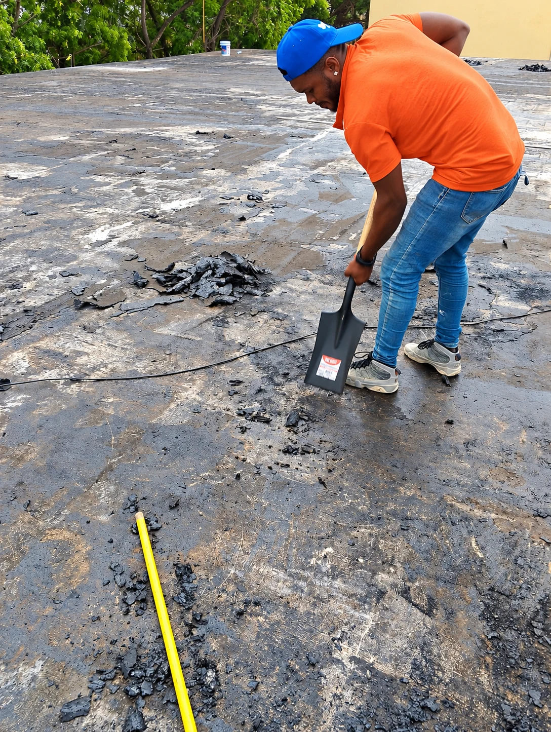 Trabajador con camiseta naranja y gorra azul retira material deteriorado de un techo con una pala.