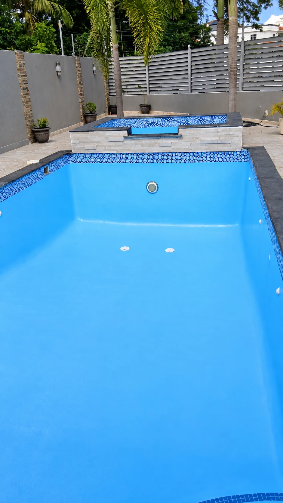 Piscina vacía de color azul con mosaicos, una pequeña área superior y revestimiento de piedra clara.